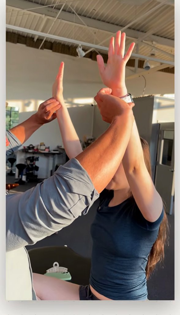 Patient holding both arms overhead while the clinician checks the pulse for the white hand sign
