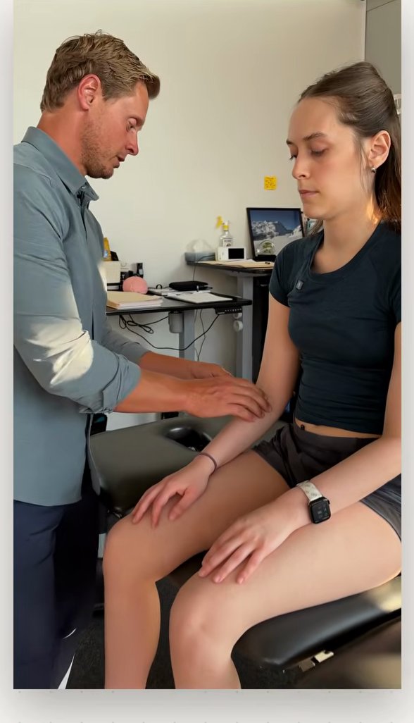 Clinician tapping a tendon reflex at the elbow of a seated patient with a reflex hammer