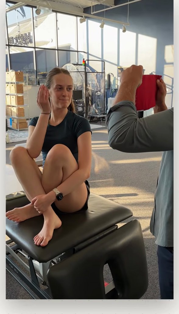 Clinician holding a red card in front of a seated patient who is comparing its brightness between her eyes