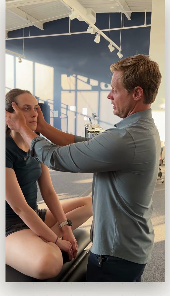 Clinician holding a seated patient's head with both hands while she keeps her eyes fixed on his nose during a vestibulo-ocular reflex test